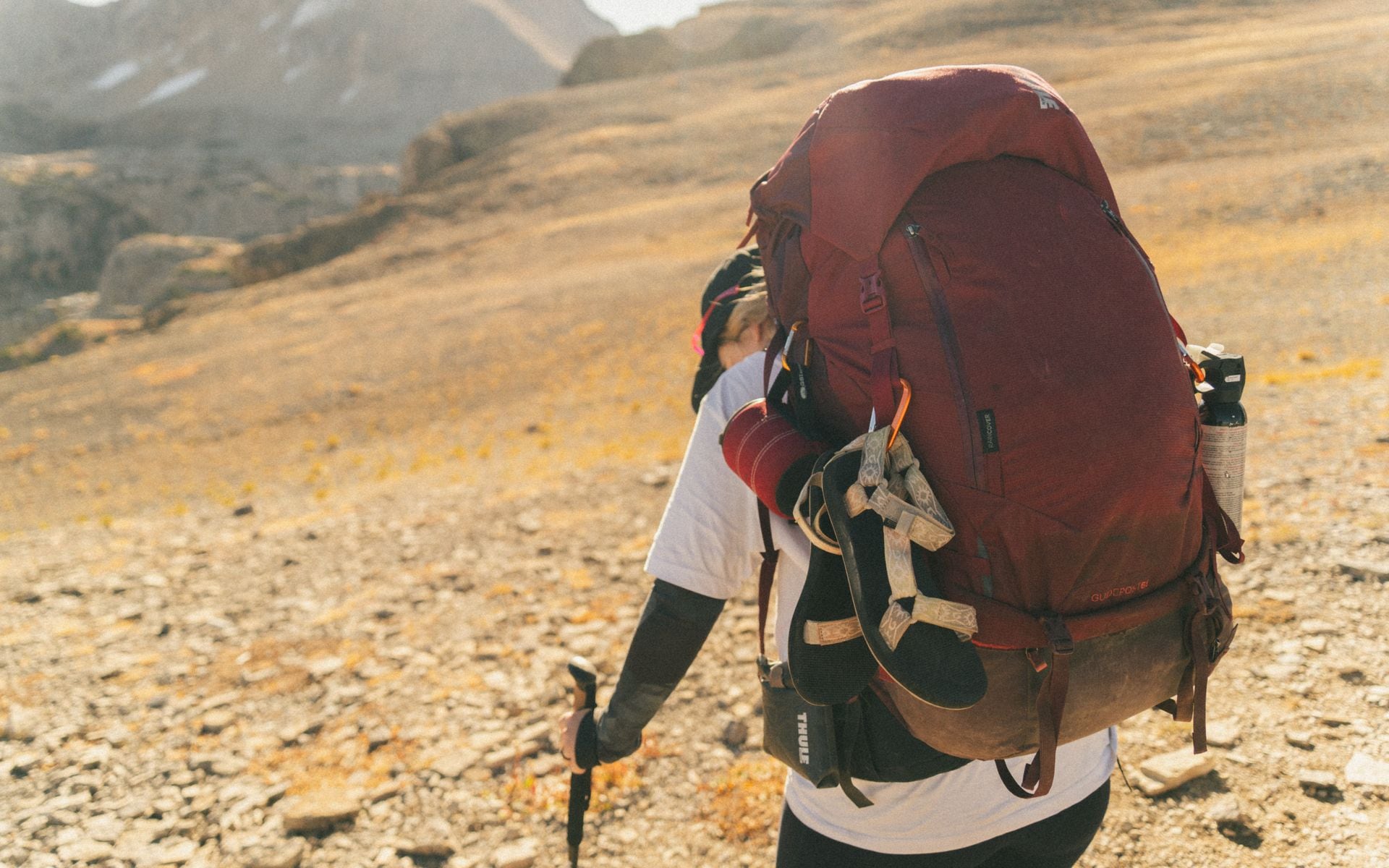 Hiker with bear spray canister on hip holster walking a trail through Wyoming's Yellowstone backcountry with open sagebrush flats ahead