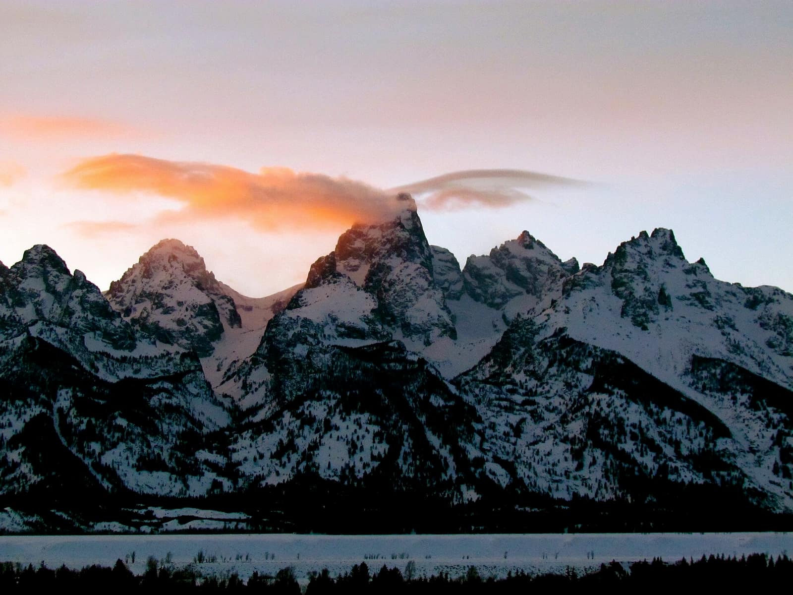 The Teton Range at sunset in winter, covered in snow, viewed across a frozen Jackson Hole valley in Wyoming