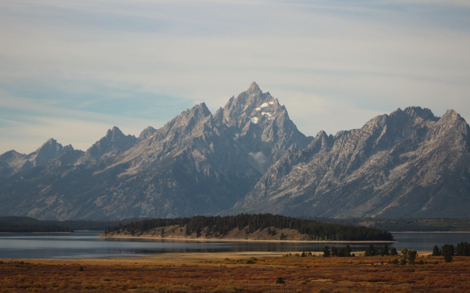 The Teton Range rising above Jackson Lake with fall foliage along the shoreline in Grand Teton National Park, Wyoming